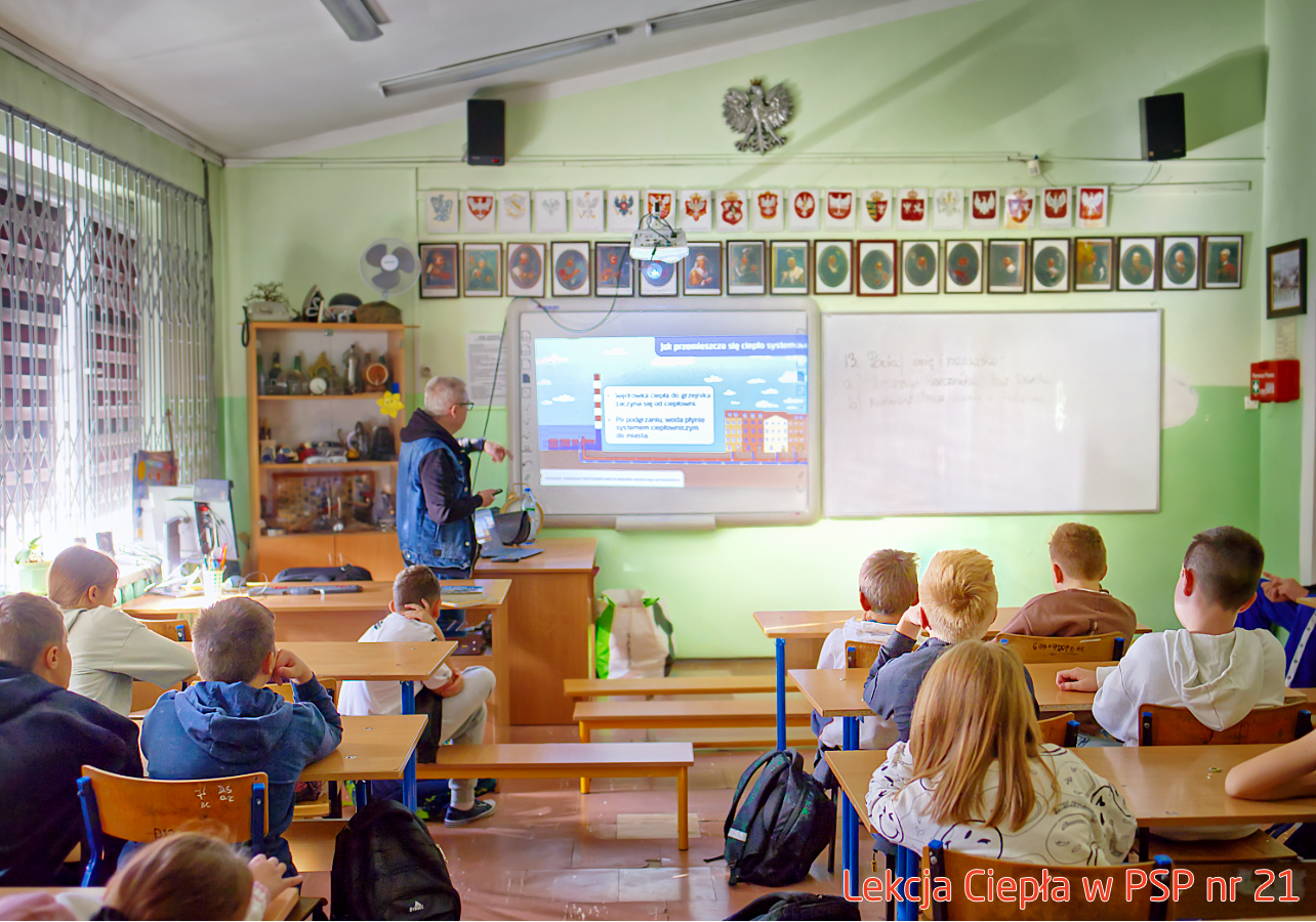 Pracownik „RADPEC” S.A. prowadzi lekcję ciepła dla uczniów klasy IV PSP nr 21. Stoi przed grupą uczniów. W tle znajduje się ekran z jednym ze slajdów prezentacji.