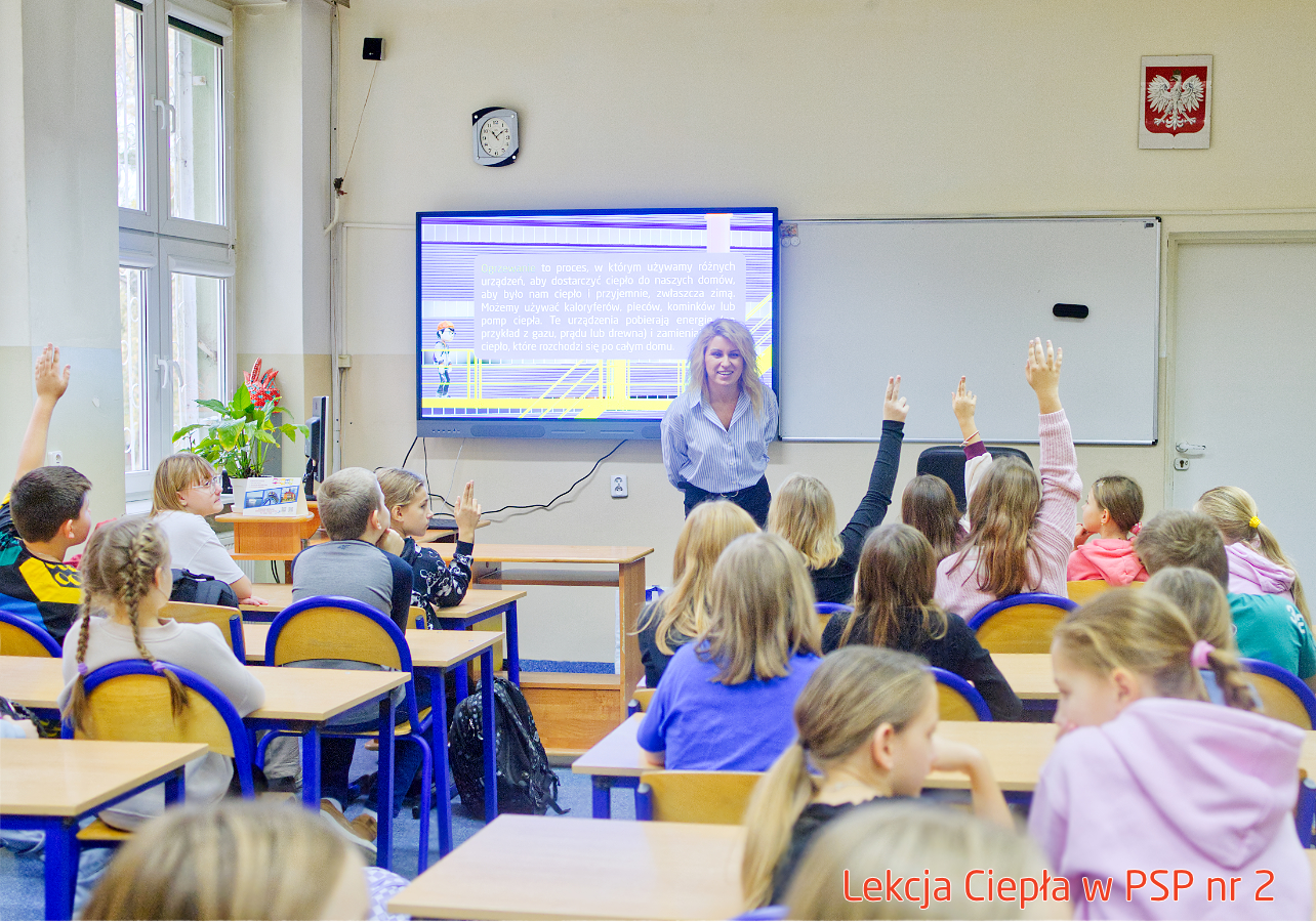 Pracownik „RADPEC” S.A. prowadzi lekcję ciepła dla uczniów klasy IV PSP nr 2. Stoi przed grupą uczniów. W tle znajduje się ekran z jednym ze slajdów prezentacji.