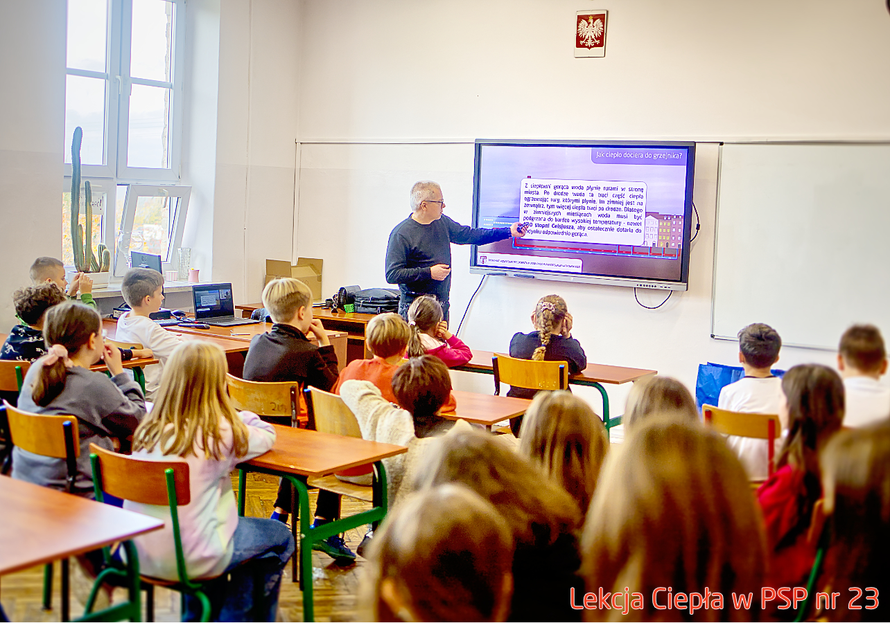 Pracownik „RADPEC” S.A. prowadzi lekcję ciepła dla uczniów klasy IV PSP nr 23. Stoi przed grupą uczniów. W tle znajduje się ekran z jednym ze slajdów prezentacji.
