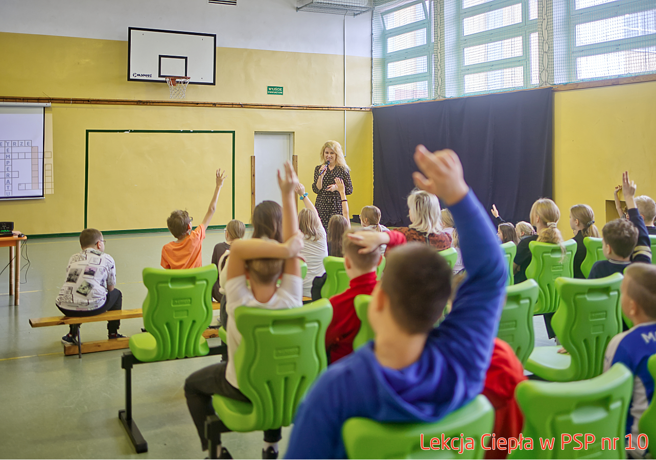 Pracownik „RADPEC” S.A. prowadzi lekcję ciepła dla uczniów klasy IV PSP nr 10. Stoi przed grupą uczniów. W tle znajduje się ekran z jednym ze slajdów prezentacji.