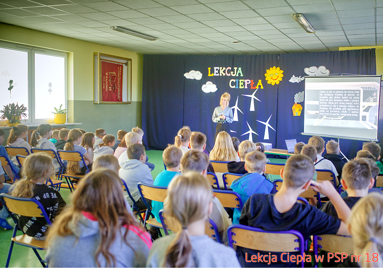 Pracownik „RADPEC” S.A. prowadzi lekcję ciepła dla uczniów klasy IV PSP nr 18. Stoi przed grupą uczniów. W tle znajduje się ekran z jednym ze slajdów prezentacji.