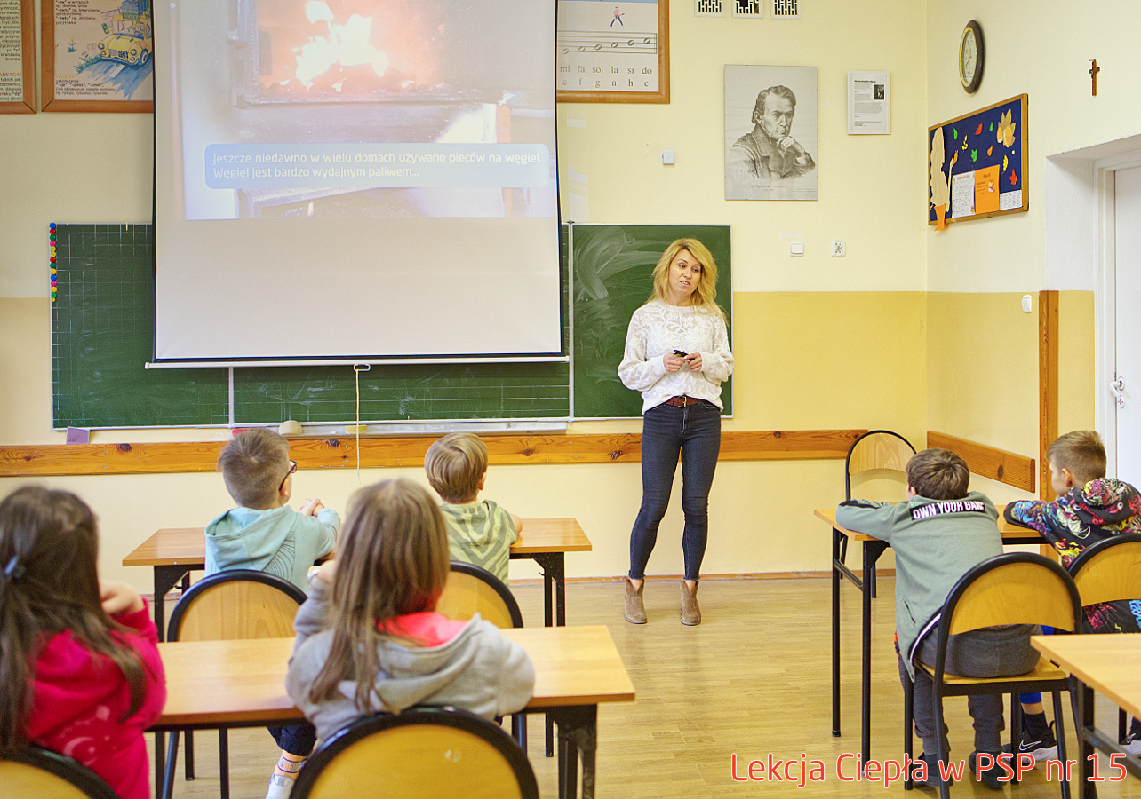 Pracownik „RADPEC” S.A. prowadzi lekcję ciepła dla uczniów klasy IV PSP nr 15. Stoi przed grupą uczniów. W tle znajduje się ekran z jednym ze slajdów prezentacji.
