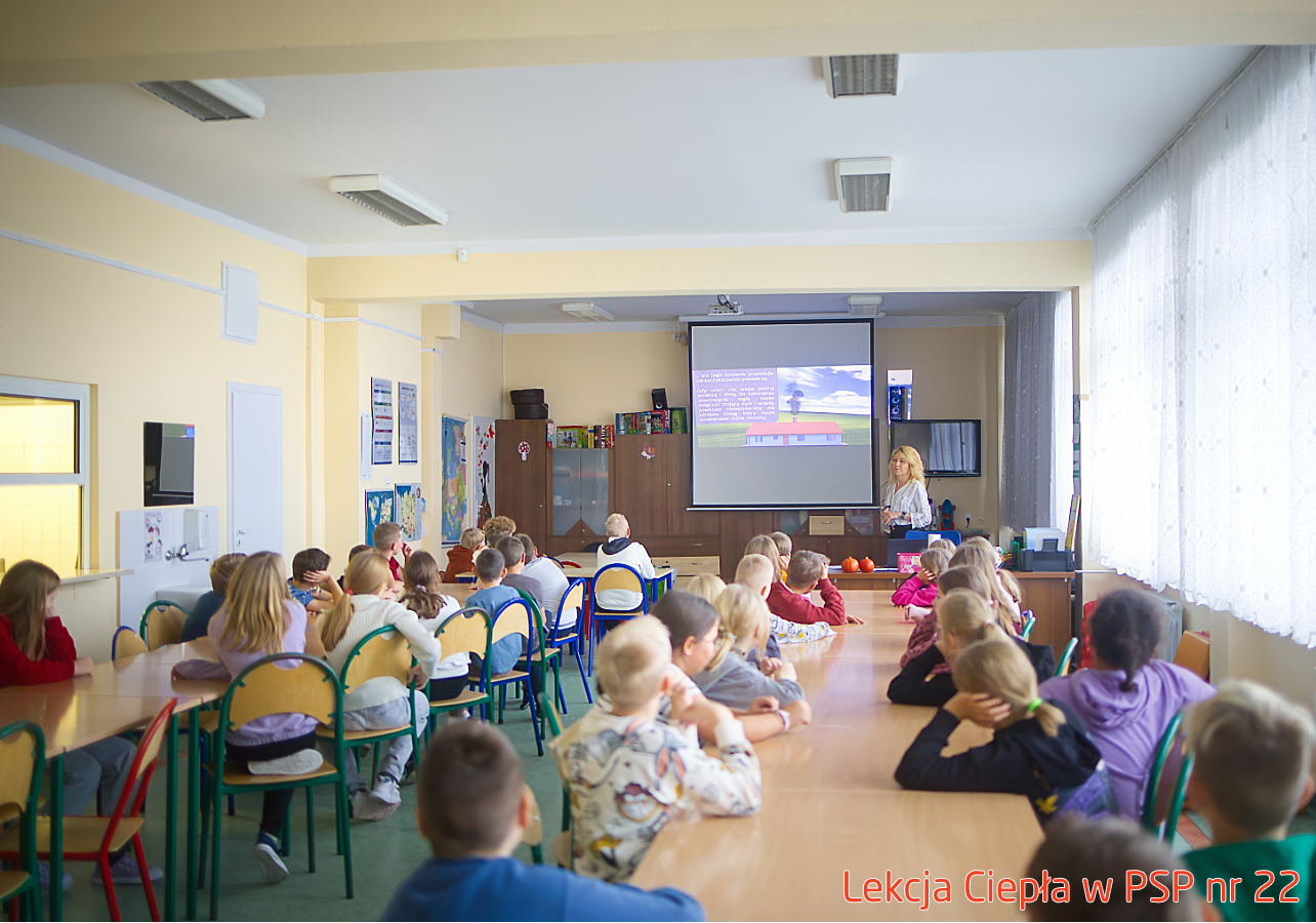 Pracownik „RADPEC” S.A. prowadzi lekcję ciepła dla uczniów klasy IV PSP nr 22. Stoi przed grupą uczniów. W tle znajduje się ekran z jednym ze slajdów prezentacji.