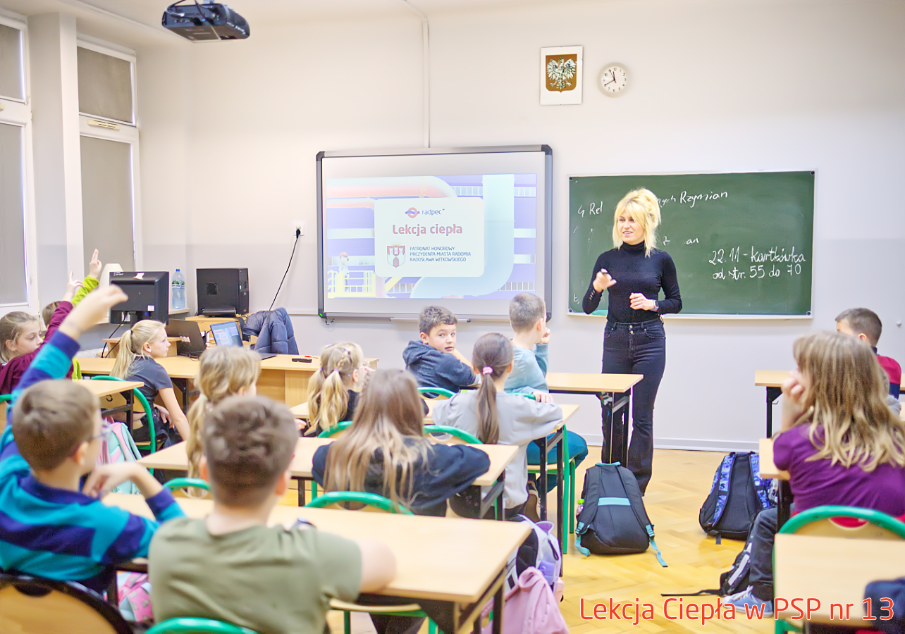 Pracownik „RADPEC” S.A. prowadzi lekcję ciepła dla uczniów klasy IV PSP nr 13. Stoi przed grupą uczniów. W tle znajduje się ekran z jednym ze slajdów prezentacji.
