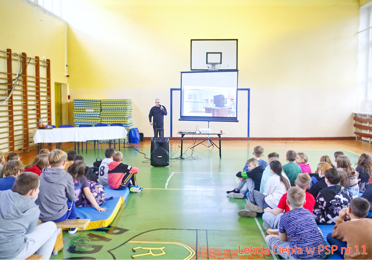 Pracownik „RADPEC” S.A. prowadzi lekcję ciepła dla uczniów klasy IV PSP nr 11. Stoi przed grupą uczniów. W tle znajduje się ekran z jednym ze slajdów prezentacji.