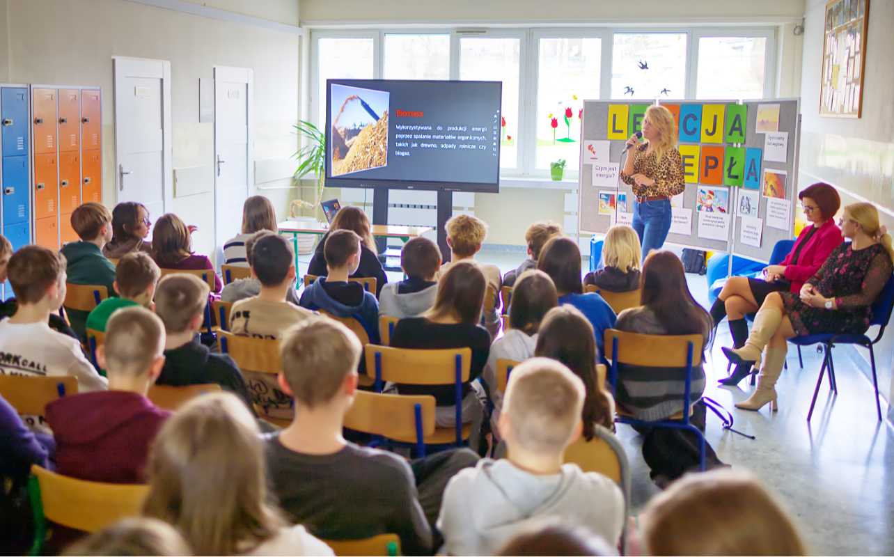 Pracownik „RADPEC” S.A. prowadzi lekcję ciepła dla uczniów klasy VI jednej z radomskich szkół. Stoi przed grupą uczniów. W tle znajduje się ekran z jednym ze slajdów prezentacji.