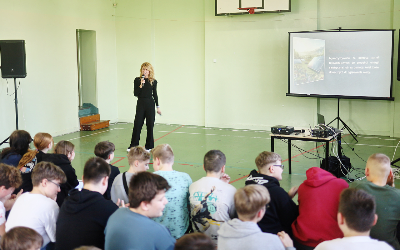Pracownik „RADPEC” S.A. prowadzi lekcję ciepła dla uczniów klasy VI jednej z radomskich szkół. Stoi przed grupą uczniów. W tle znajduje się ekran z jednym ze slajdów prezentacji.