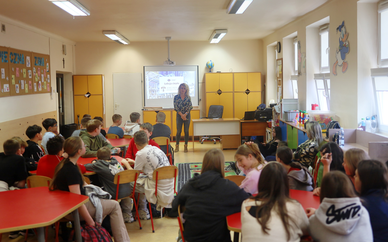 Pracownik „RADPEC” S.A. prowadzi lekcję ciepła dla uczniów klasy VI jednej z radomskich szkół. Stoi przed grupą uczniów. W tle znajduje się ekran z jednym ze slajdów prezentacji.