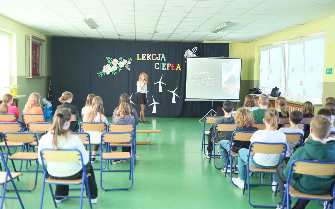 Pracownik „RADPEC” S.A. prowadzi lekcję ciepła dla uczniów klasy VI jednej z radomskich szkół. Stoi przed grupą uczniów. W tle znajduje się ekran z jednym ze slajdów prezentacji.