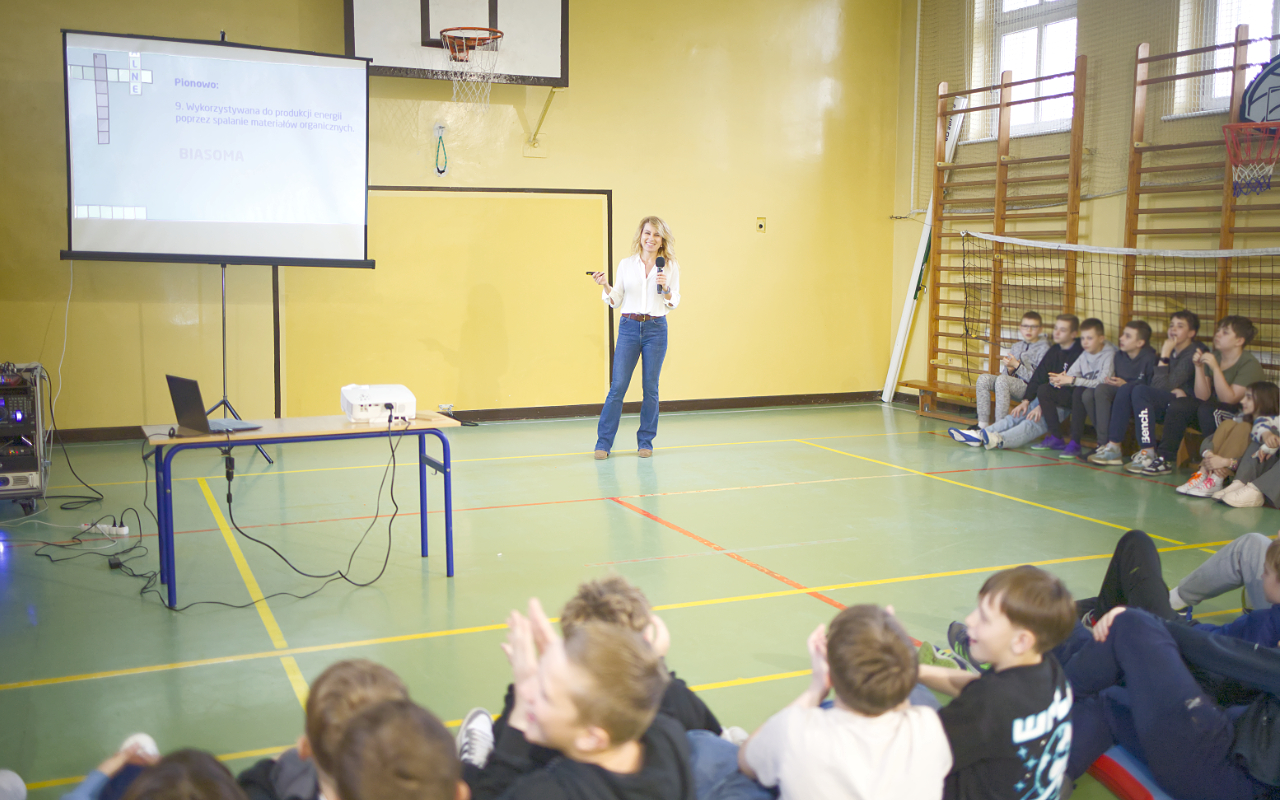Pracownik „RADPEC” S.A. prowadzi lekcję ciepła dla uczniów klasy VI jednej z radomskich szkół. Stoi przed grupą uczniów. W tle znajduje się ekran z jednym ze slajdów prezentacji.
